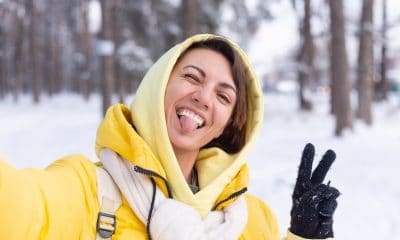 young beautiful happy cheerful woman in the winter forest video blog, makes a selfie photo against the background of beautiful snow, smiles, dressed in warm clothes, yellow bright jacket