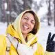 young beautiful happy cheerful woman in the winter forest video blog, makes a selfie photo against the background of beautiful snow, smiles, dressed in warm clothes, yellow bright jacket
