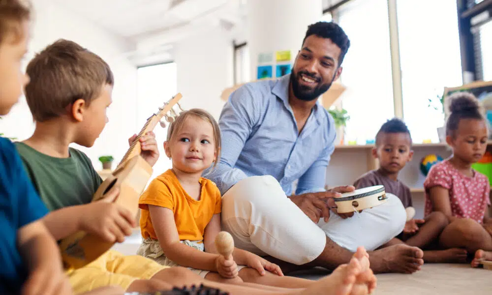 group of small nursery school children with man teacher sitting on floor indoors in classroom, playing.